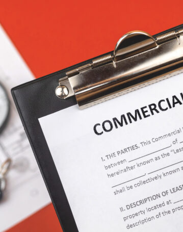 Man holds commercial lease agreement in hand. Clipboard with official document. Background with real property papers and house key